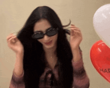 a woman wearing sunglasses is holding her hair in front of balloons that say happy birthday