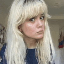 a woman with blonde hair and a blue shirt looks at the camera
