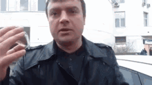 a man in a black leather jacket is holding a glass of water .