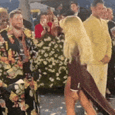 a woman in a red dress is standing in front of a crowd of people wearing yellow suits .