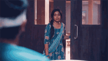 a woman in a blue dress is standing in a doorway looking at a man in a blue shirt .