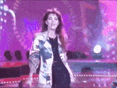 a woman in a colorful jacket is standing on a stage