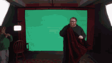 a man is standing in front of a green screen while holding a red blanket