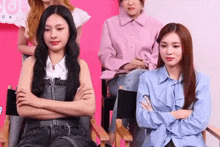 two women are sitting in chairs with their arms crossed and looking at the camera .