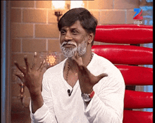 a man with a white beard is sitting in front of a screen that says zee tv