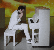 a man in a white suit sits on a bench playing a piano