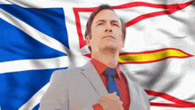 a man in a suit and tie stands in front of a newfoundland and labrador flag