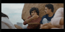 a group of young men are sitting on a rock talking