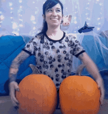 a woman wearing a shirt with skulls on it holds two pumpkins