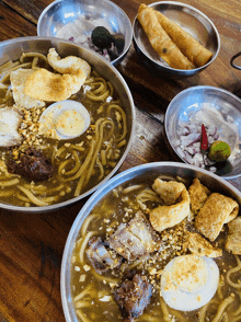 two bowls of noodles with meat and eggs are on a wooden table