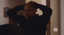 a bald man is holding his head with his hands .