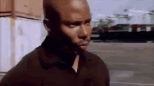 a man in a black shirt is standing in a parking lot looking at the camera .