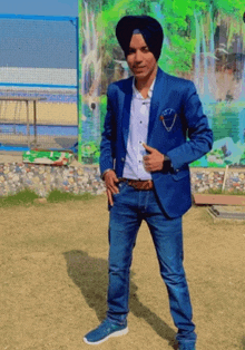 a man wearing a turban and a blue jacket is standing in front of a waterfall