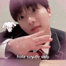 a man in a suit and tie is sitting at a table and says hola soy de valy