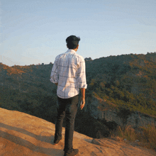 a man in a plaid shirt stands on a rocky hillside