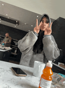 a woman in a hoodie giving a peace sign in a kitchen