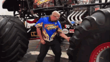 a man standing in front of a monster truck wearing a shirt that says " stone crusher "