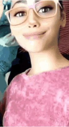 a girl wearing glasses and a pink shirt is smiling and taking a selfie .