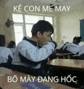 a man sitting at a desk in a classroom with the words ke con me may bo may dang hoc