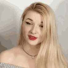 a blonde woman wearing red lipstick and a necklace looks at the camera