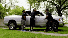 a group of men are standing around a silver truck