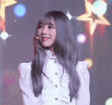 a woman with long gray hair and a white shirt is standing in front of a stage with stars in the background .