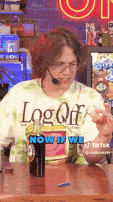 a man wearing a shirt that says log off is sitting at a table