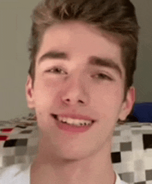 a young man is smiling and looking at the camera while wearing a white shirt .