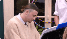 a man in a tan sweater sits at a keyboard