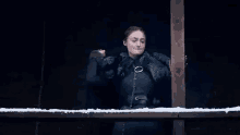 a woman in a black coat is standing next to a wooden railing in a dark room .