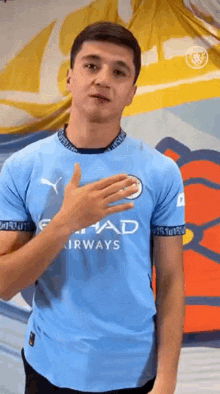 a man in a blue t-shirt is standing in front of a wall with his hand on his chest .