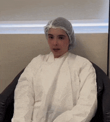 a woman wearing a white gown and a plastic cap is sitting in a chair