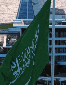 a green flag with arabic writing on it flies in front of a building
