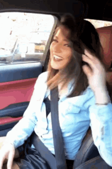 a woman wearing a seat belt is sitting in a car and smiling