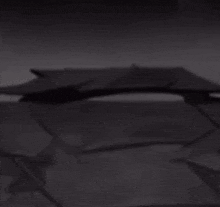 a black and white photo of a cartoon cat sitting on a table next to a laptop .
