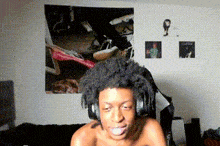 a shirtless man wearing headphones is sitting in front of a wall with a picture of a man on it