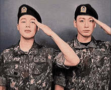 two men in military uniforms salute in front of a black wall