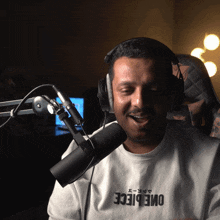 a man wearing headphones and a shirt that says one piece is smiling in front of a microphone