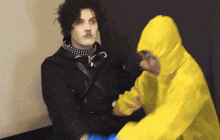 a man in a black jacket is talking to another man in a yellow hooded jacket