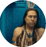 a man with long hair and feathers on his head is sitting in a blue circle .