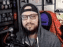 a man with a beard and glasses is wearing a hoodie and a hat .