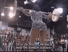 a woman in a zebra print shorts is lifting a barbell in front of a crowd .
