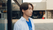 a young man wearing a blue t-shirt and a white shirt is standing in front of a building .