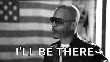 a man wearing sunglasses and a leather jacket is saying `` i 'll be there '' in front of a flag .