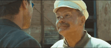 a man with a mustache wearing a hat and sunglasses talks to another man