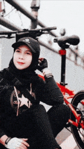 a woman in a hijab sits next to a red bike