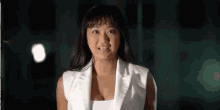 a woman in a white vest is standing in the dark and smiling .