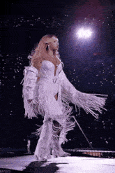 a woman is walking on a stage wearing a white fringed outfit .