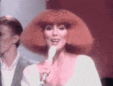 a woman with red hair is singing into a microphone while a man stands behind her .