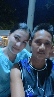 a man and a woman posing for a picture and the man is wearing a blue shirt with a dragon on the front